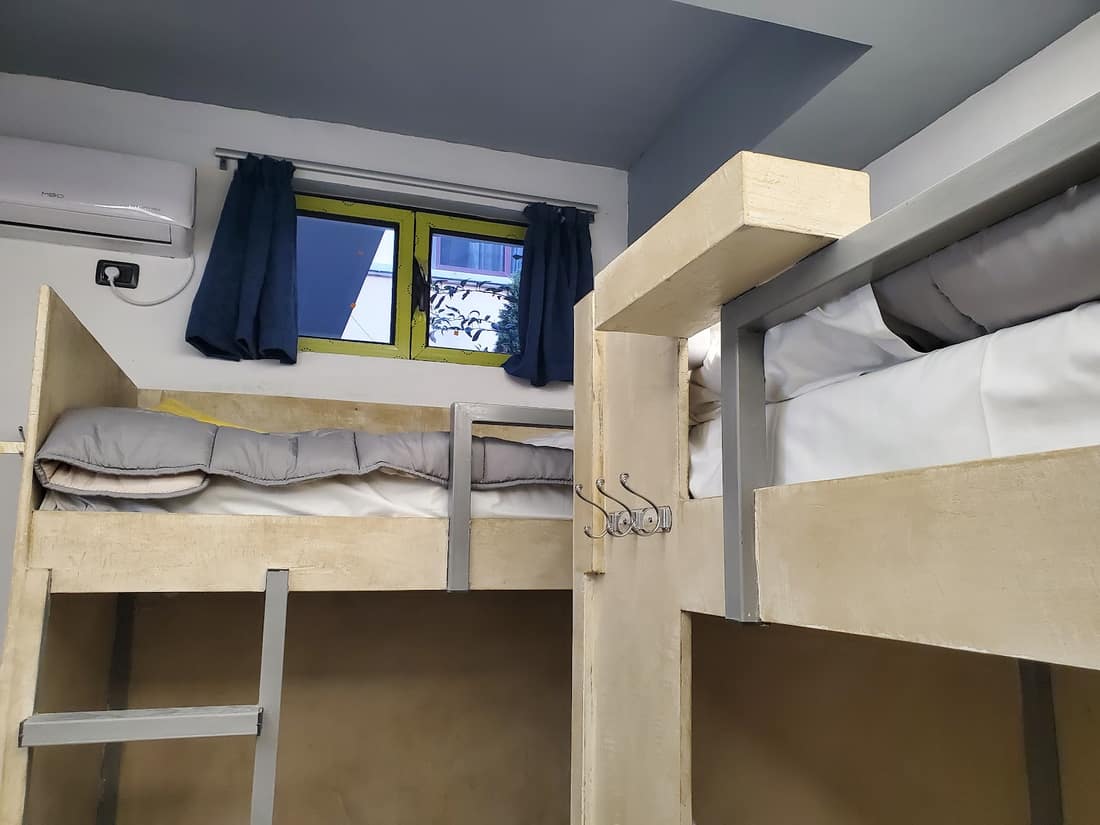 Pale wood bunk beds with hooks, a ladder and a window with blue curtains