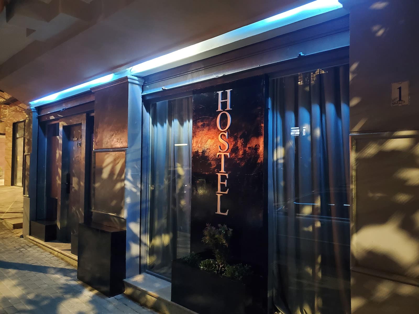 Wander Luxe Hostel at night: dark facade lit by a blue neon strip, with HOSTEL lettered vertically in the window